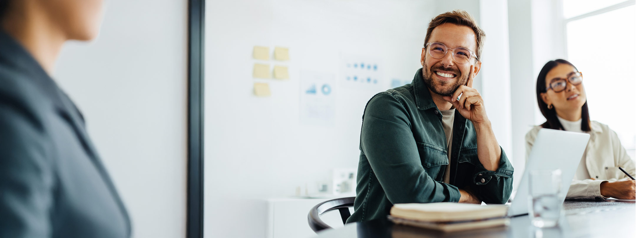 A photo of a middle aged man smiling while sitting at a table during a meeting.